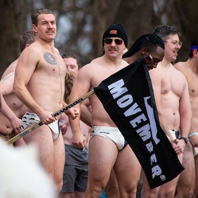 Photo of athletic men in Movember-branded swimwear, about to plunge into frigid water.