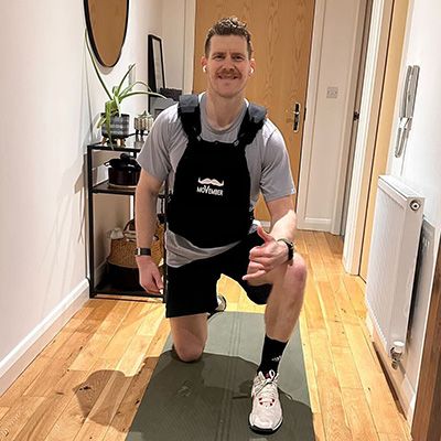 Athletic man, wearing a weighted vest and sports attire, looking to camera.