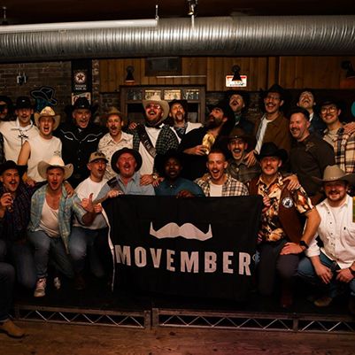 Photo of cheering Movember supporters at a bar, holding up a Movember-branded flag